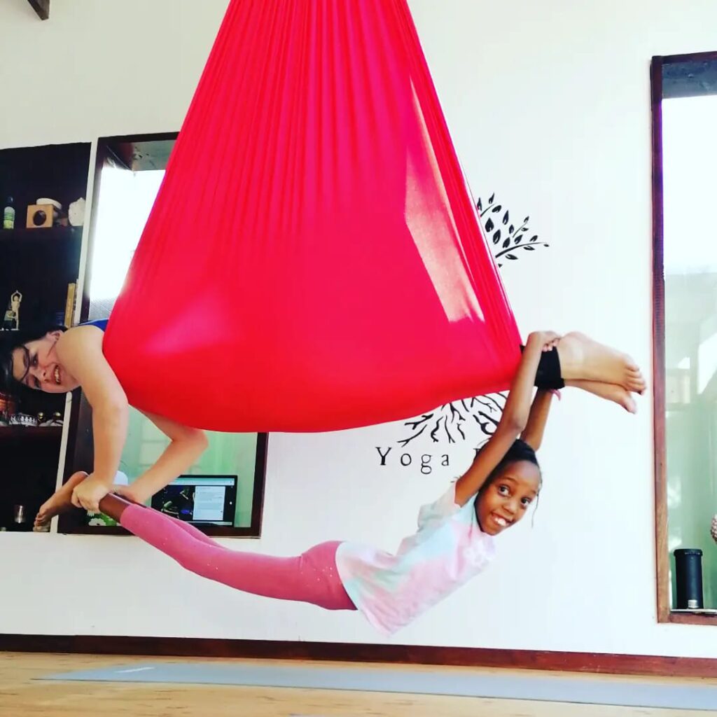 Yoga instructor guiding child in aerial hammock